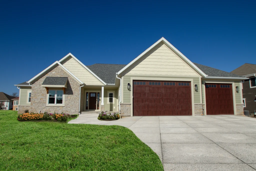 A modern suburban house with stone and wood facade, manicured lawn, flower beds, and a three-car garage under a clear blue sky.
