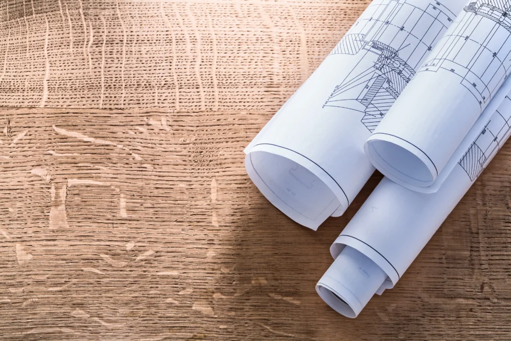 Three rolled architectural blueprints on a wooden table depict engineering designs, showcasing detailed technical drawings and plans for construction projects.